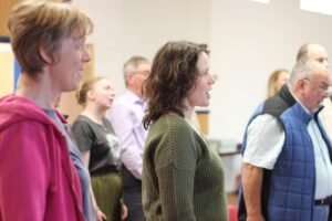 Choir members standing in sections during warm up at rehearsal, singing together and watching conductor, Classical Choir, Birmingham UK